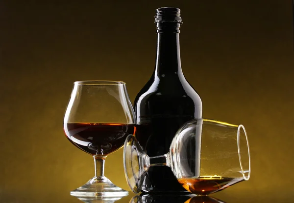 Bicchieri di brandy e bottiglia su sfondo giallo — Foto Stock