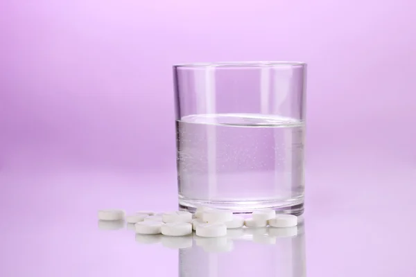 Glas vatten och piller på lila bakgrund — Stockfoto