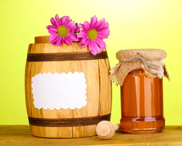 stock image Sweet honey in jar and barrel with drizzler on wooden table on green background