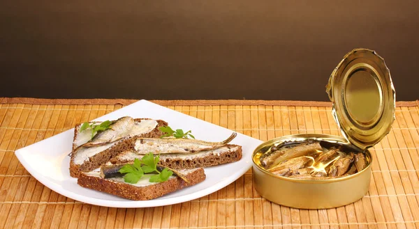 stock image Tasty sandwiches with sprats on plate on wooden mat on brown background