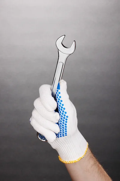 Skiftnyckel i handen med skydd handske på grå bakgrund — Stockfoto