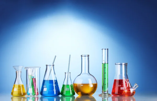 Diferentes cristalería de laboratorio con líquido de color y con reflexión sobre fondo azul —  Fotos de Stock