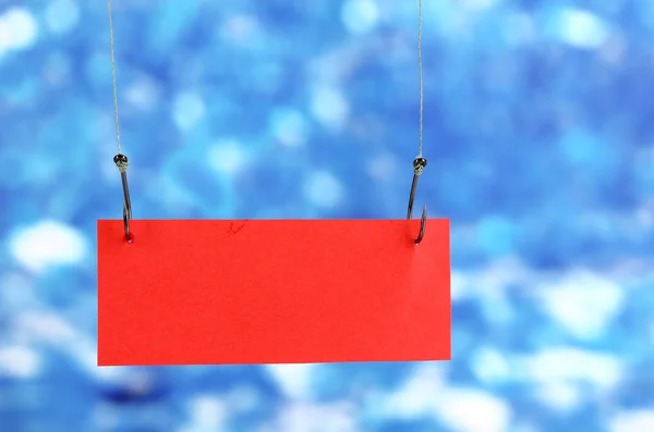 Пустой лист бумаги на рыболовных крючках на синем фоне — стоковое фото
