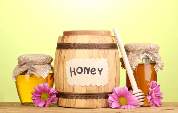 Süßer Honig in Fässern und Gläsern mit Nieselregen auf Holztisch auf grünem Hintergrund — Stockfoto