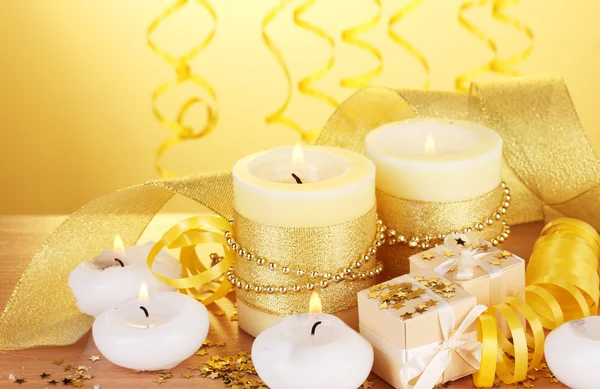 Красивые свечи, подарки и декор на деревянном столе на желтом фоне — стоковое фото