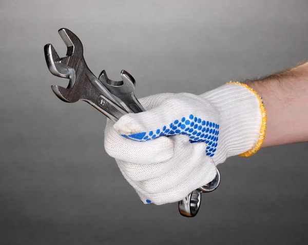 Wrenches in hand with protection glove on grey background — Stock Photo, Image