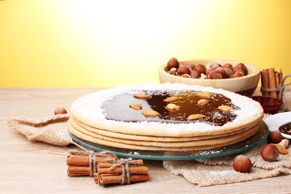 Cake on glass stand and nuts on wooden table on yellow background — Stock Photo, Image