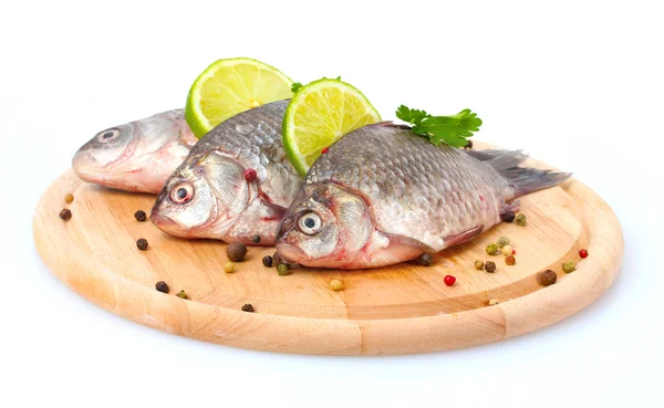 Свежие рыбы с лаймом, петрушкой и специями на деревянной разделочной доске, изолированной на белом — стоковое фото