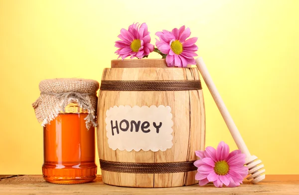 Γλυκό μέλι στο βαρέλι και βάζο με drizzler στο ξύλινο τραπέζι σε κίτρινο φόντο — Φωτογραφία Αρχείου