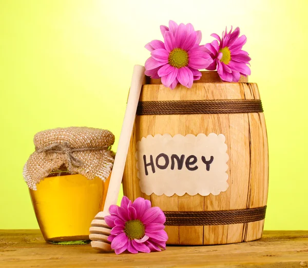 Miel dulce en barril y tarro con rociador sobre mesa de madera sobre fondo verde —  Fotos de Stock