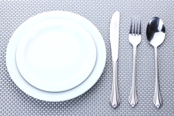 Platos blancos vacíos con tenedor, cuchara y cuchillo sobre un mantel gris —  Fotos de Stock