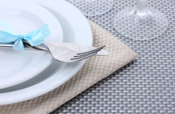 Piatti bianchi vuoti, forchetta e coltello legati con un nastro e bicchieri su una tovaglia grigia — Foto Stock