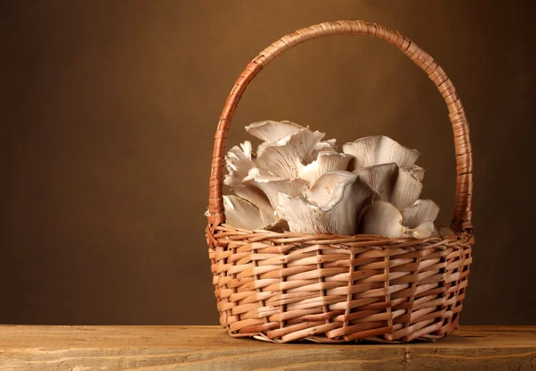 Stock image Oyster mushrooms in basket on wooden table on brown background