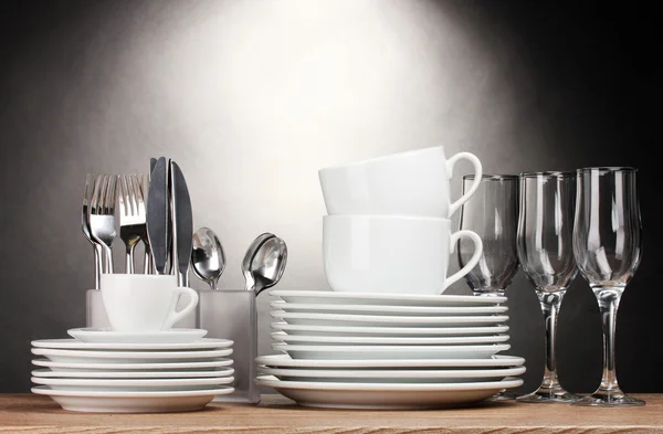 Piatti puliti, bicchieri, tazze e posate su tavolo in legno su fondo grigio — Foto Stock