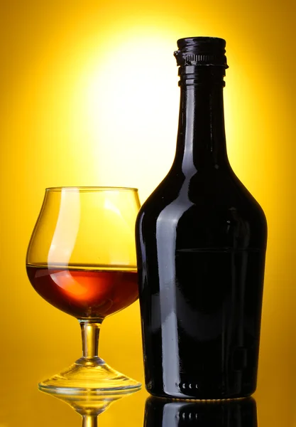 Glas brandy en fles op gele achtergrond — Stockfoto