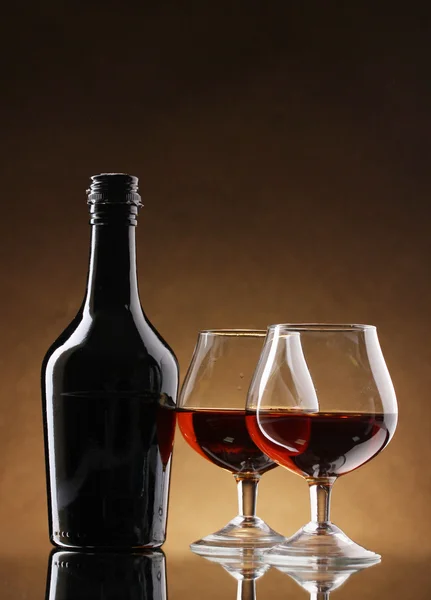 Vasos de brandy y botella sobre fondo marrón — Foto de Stock