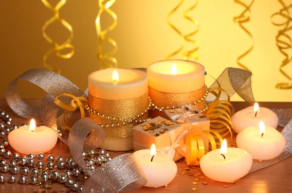 Красивые свечи, подарки и декор на деревянном столе на желтом фоне — стоковое фото