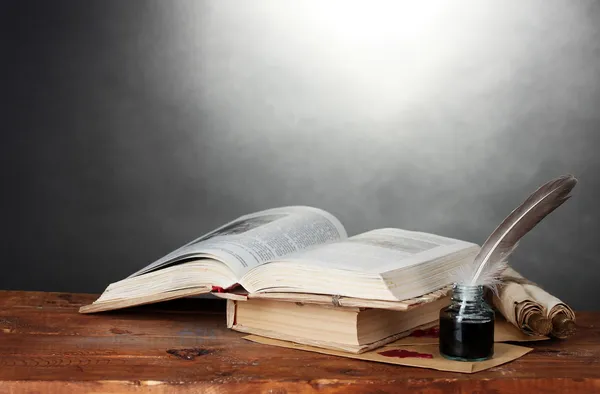 Старые книги, свитки, перо и чернильница на деревянном столе на сером фоне — стоковое фото