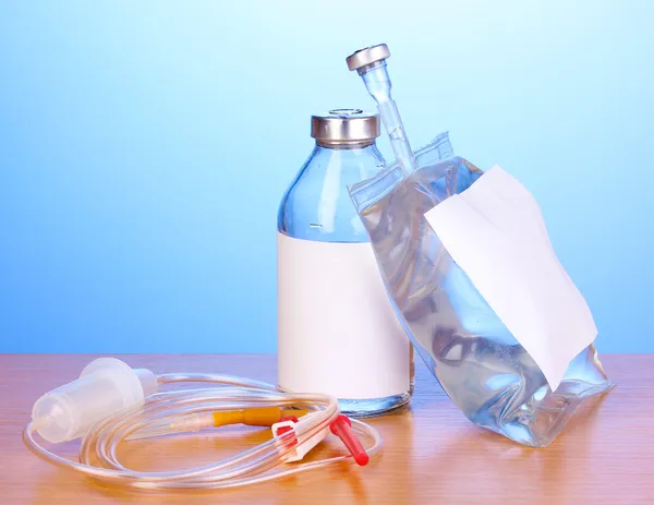 Botella y bolsa de antibióticos intravenosos y juego de infusión de plástico sobre mesa de madera sobre fondo azul —  Fotos de Stock