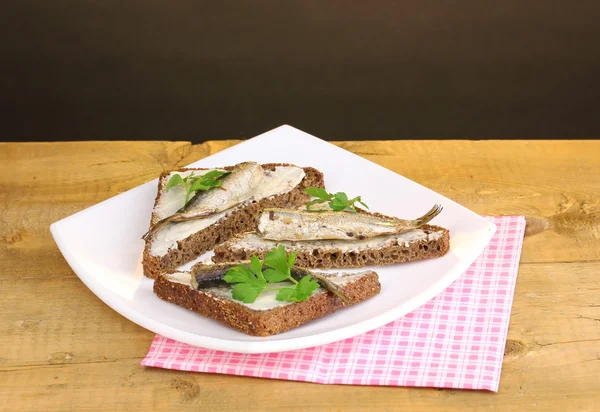 Sabrosos sándwiches con espadines en plato sobre mesa de madera sobre fondo marrón —  Fotos de Stock