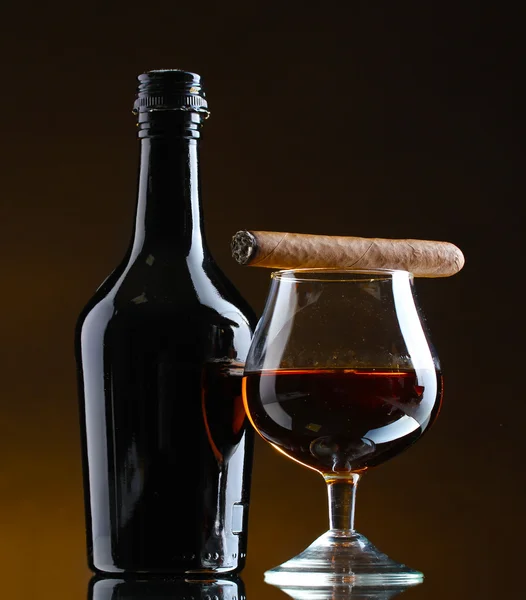 Bottle and glass of brandy and cigar on brown background — Stock Photo, Image