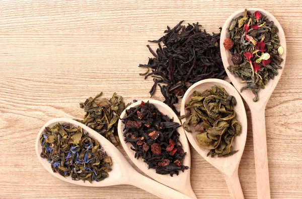 Diversi tipi di tè verde e nero secco in cucchiai su sfondo di legno — Foto Stock