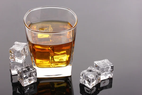 stock image Glass of scotch whiskey and ice on grey table