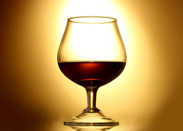 Glass of cognac on yellow background — Stock Photo, Image