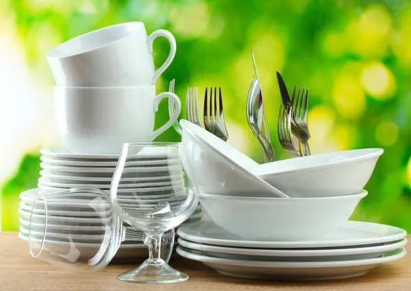 Sauberes Geschirr auf Holztisch auf grünem Hintergrund — Stockfoto