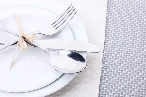 Platos blancos vacíos con tenedor, cuchara y cuchillo atados con una cinta sobre un mantel gris —  Fotos de Stock