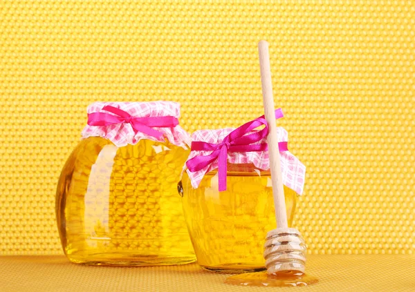 Jars of honey and wooden drizzler on yellow honeycomb background Royalty Free Stock Images
