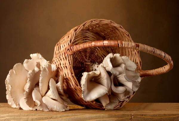 Cogumelos de ostra na cesta na mesa de madeira no fundo marrom — Fotografia de Stock