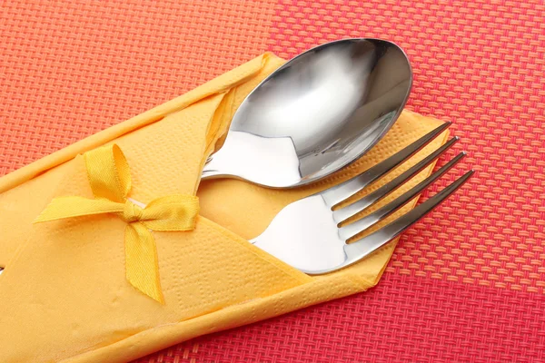 Tenedor y cuchara en un paño amarillo con un lazo sobre un mantel rojo —  Fotos de Stock