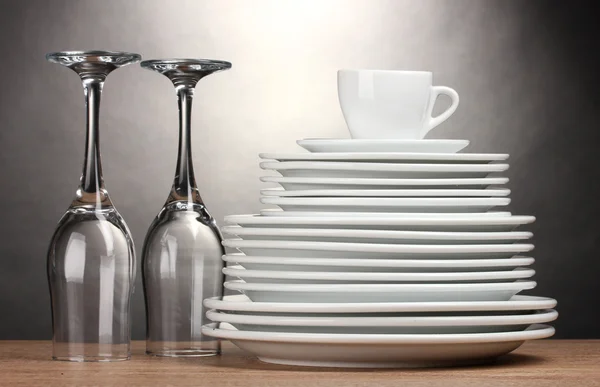 Tiszta, tányérok, poharak és kupa fából készült asztal-szürke háttér — Stock Fotó