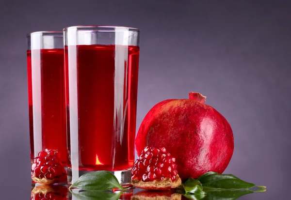Ripe pomergranate and glasses of juice on purple background — Stock Photo, Image