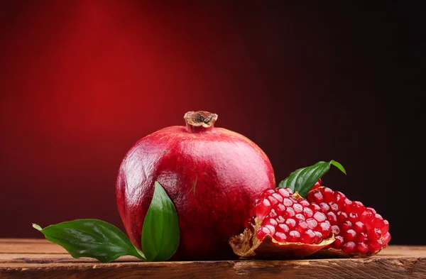 Fruta de granada madura con hojas sobre mesa de madera sobre fondo rojo —  Fotos de Stock