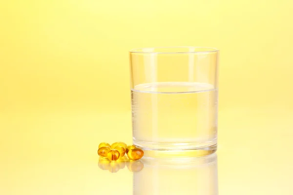 Стакан воды и таблетки на желтом фоне — стоковое фото