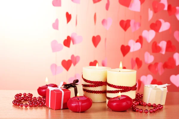 Beautiful candles with romantic decor on a wooden table on a red background Stock Photo