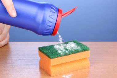 Sponge with scouring powder on wooden table on blue background clipart