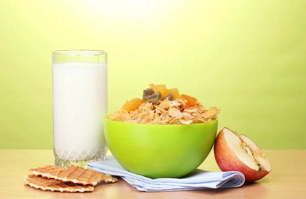Välsmakande cornflakes i grön skål, äpple och glas mjölk på träbord på grön bakgrund — Stockfoto