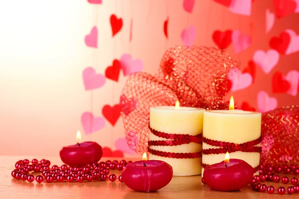 Красивые свечи с романтическим декором на деревянном столе на красном фоне — стоковое фото