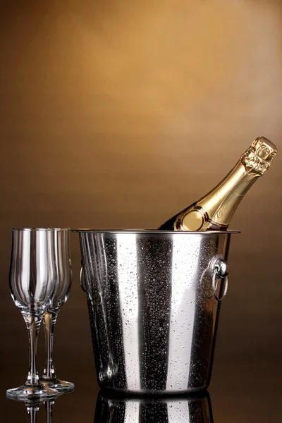 Bottiglia di champagne in secchio e calici su fondo marrone — Foto Stock
