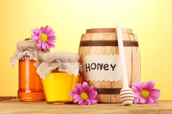 Miel dulce en barril y frascos con rociador sobre mesa de madera sobre fondo amarillo — Foto de Stock