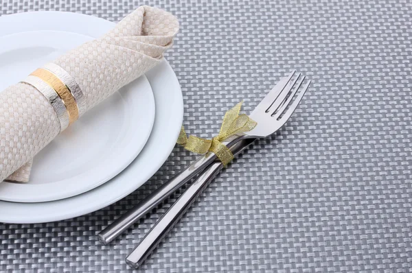 Белые пустые тарелки с вилкой и ножом, завязанные лентой на серой скатерти — стоковое фото