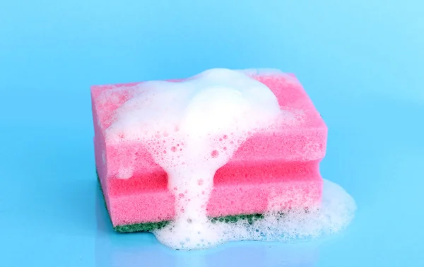 Sponge with foam of dishwashing liquid on blue background — Stock Photo, Image