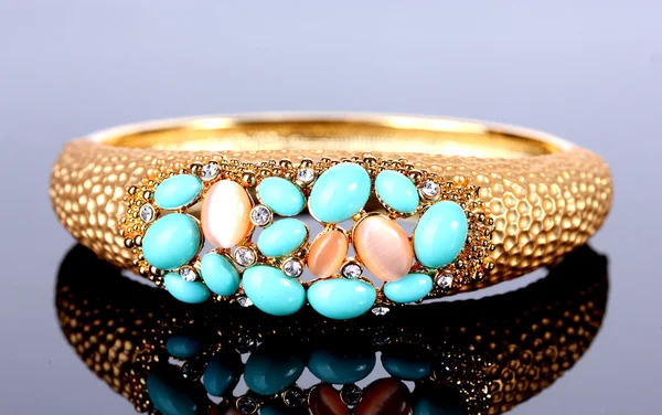 Bela pulseira dourada com pedras preciosas no fundo cinza — Fotografia de Stock