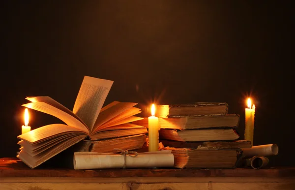 Купка старих книг зі свічкою і прокруткою в темряві — стокове фото
