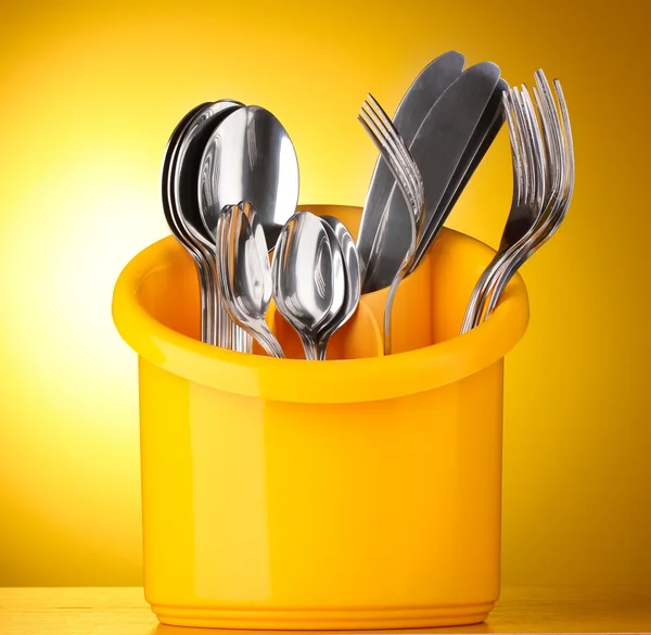 Kitchen cutlery, knives, forks and spoons in yellow stand on yellow background — Stock Photo, Image
