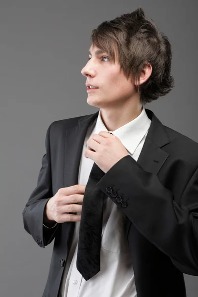 Genç işadamı gri arka plan üzerinde siyah takım elbise rahat kravat — Stok fotoğraf