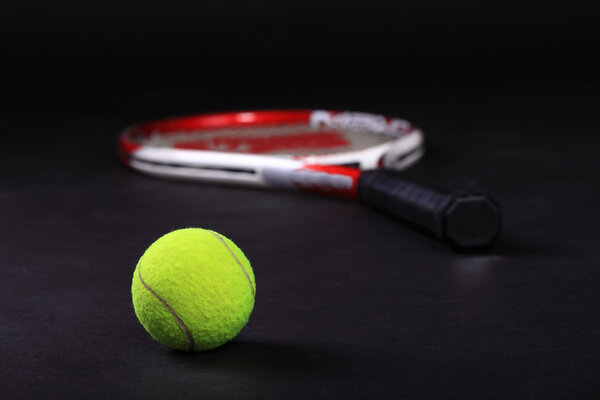 Теннисная ракетка и мячи на черном фоне
